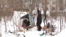Doi oameni dorm sub cerul liber, în corturi improvizate, în timp ce orașul trece nepăsător pe lângă ei